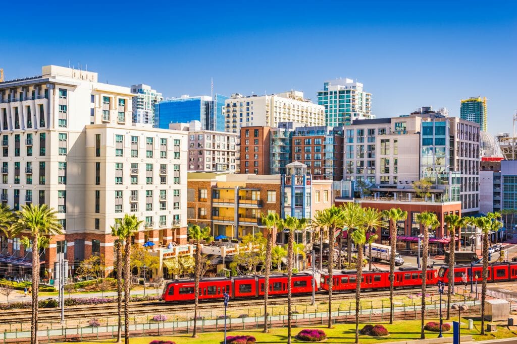 Red trolley traversing across a cityscape on a bright and vibrant day in San Diego, CA