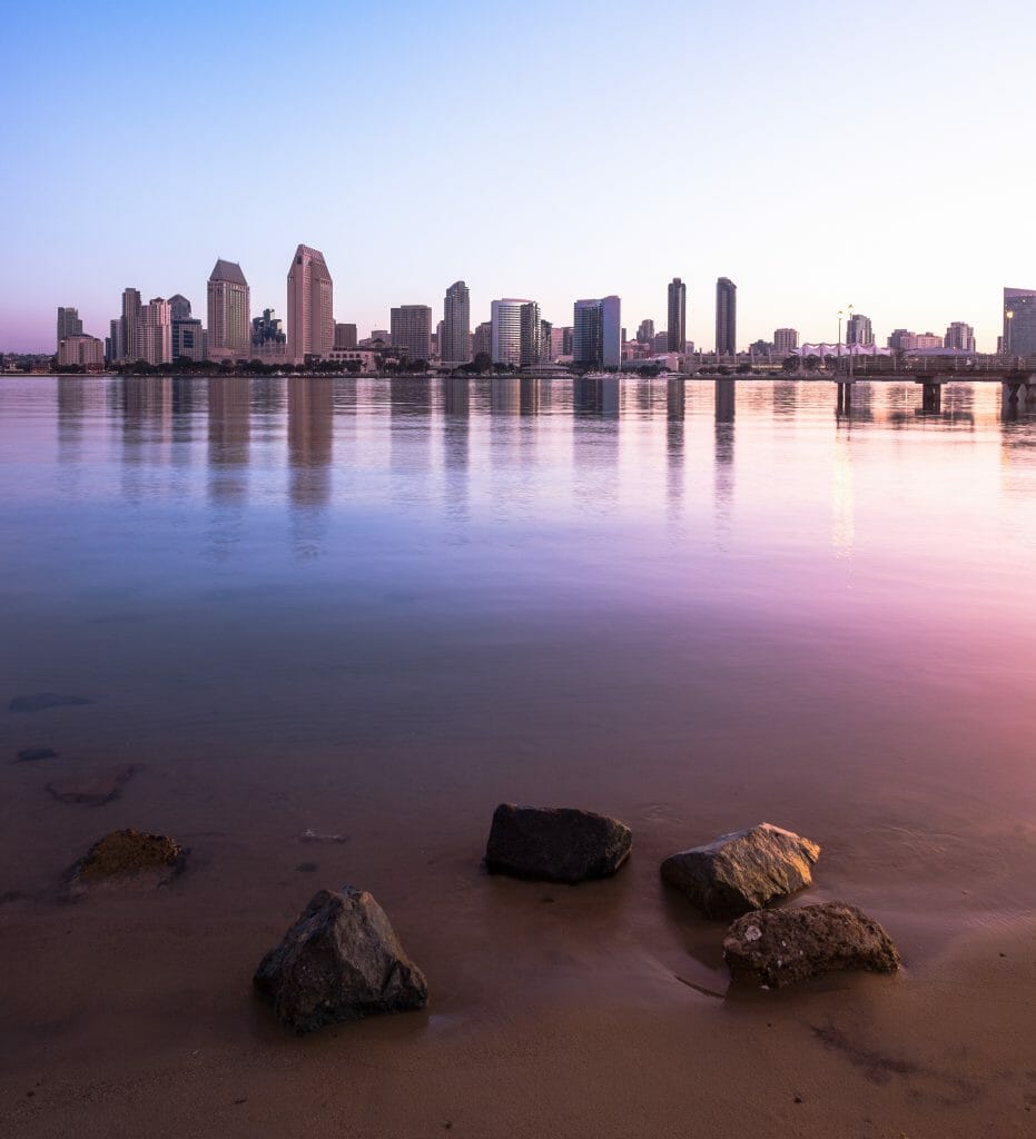 The hues of blue and purple reflect off the calm water with the city in the distance