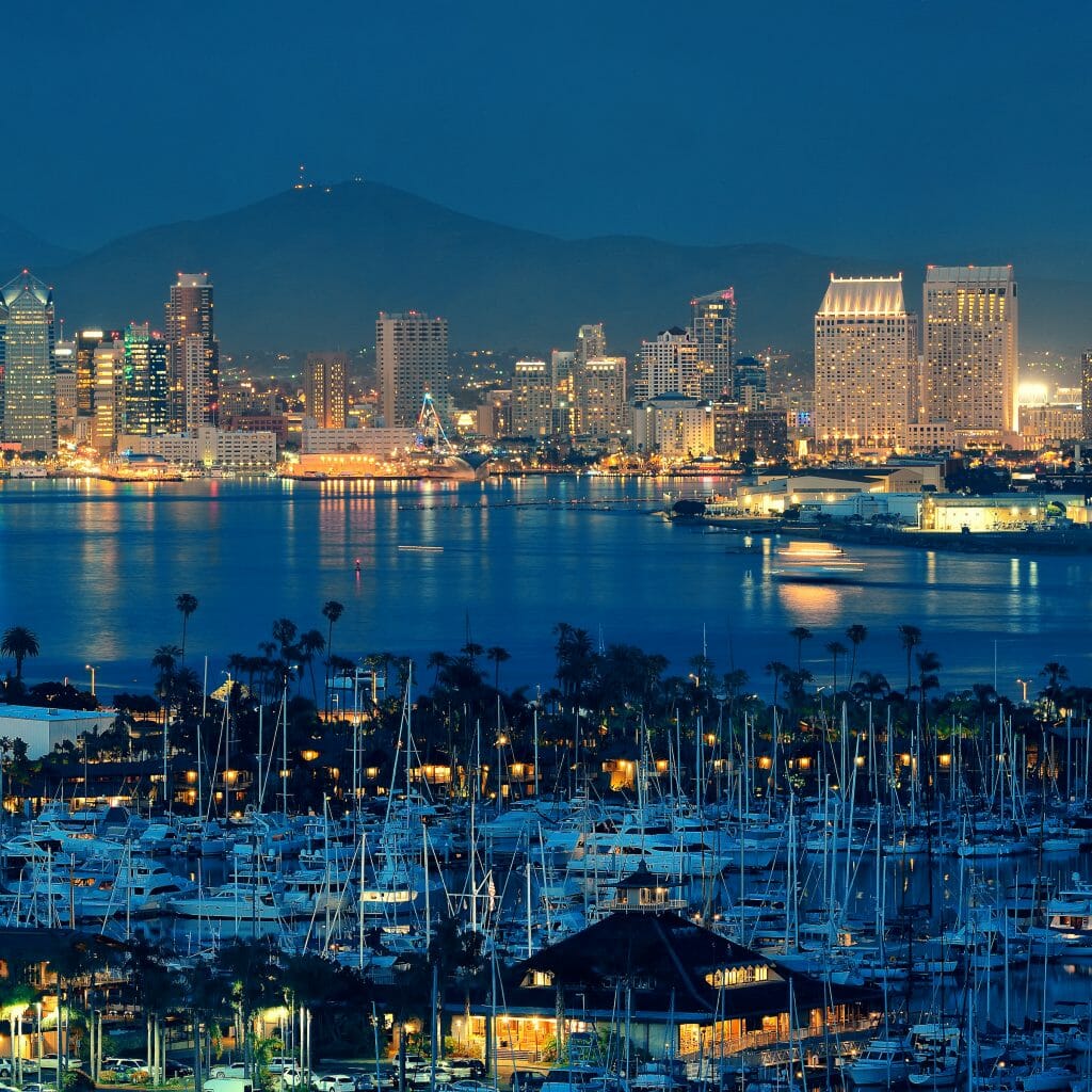 In the late evening glow, the lights dance across the downtown buildings and reflect on the bay water, hitting the boats that rest there