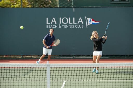 Two white people playing tennis in the bright sun