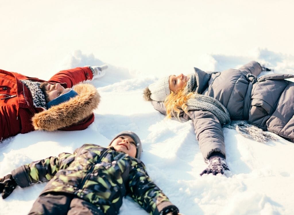 Two adults (man and woman) and a child lying in the snow making snow angels