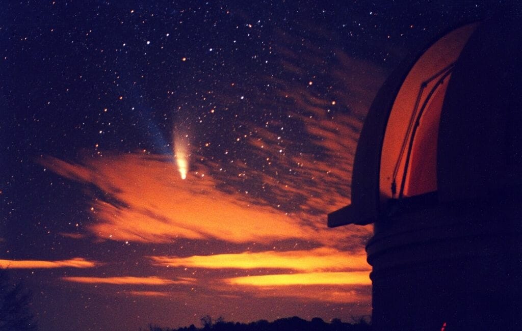 Night sky with orange sunset and starry sky, Hale Bob Comet in the center right and a part of the dome of Palomar Observatory o the right of the image