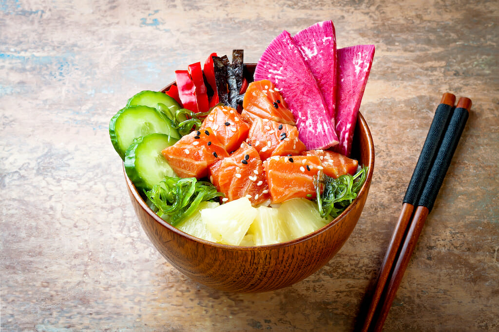 Hawaiian salmon poke bowl with seaweed, watermelon radish, cucumber, pineapple and sesame seeds. Copy space background, overhead, flat lay