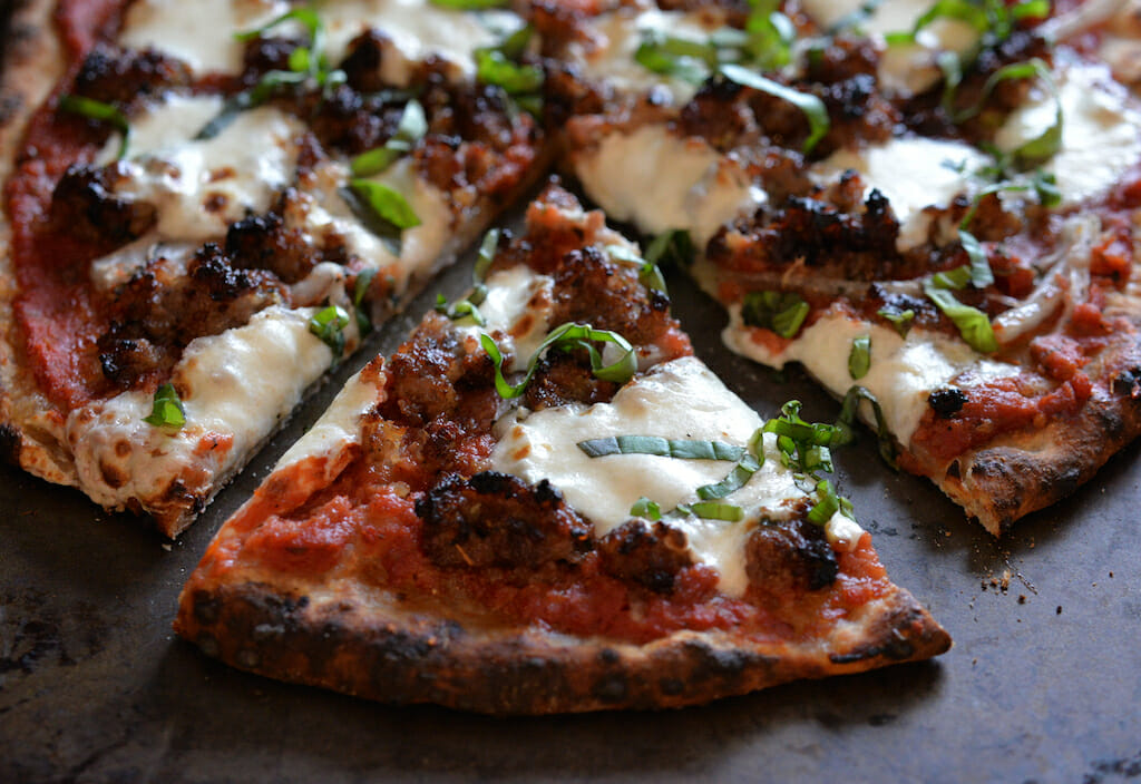 Closeup of artisanal wood fired pizza with sausage, mozzarella and basil