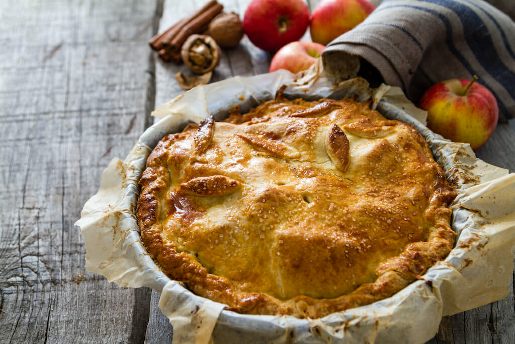 Apple pie with apples, cinnammon and nuts, rustic wood background, copy space