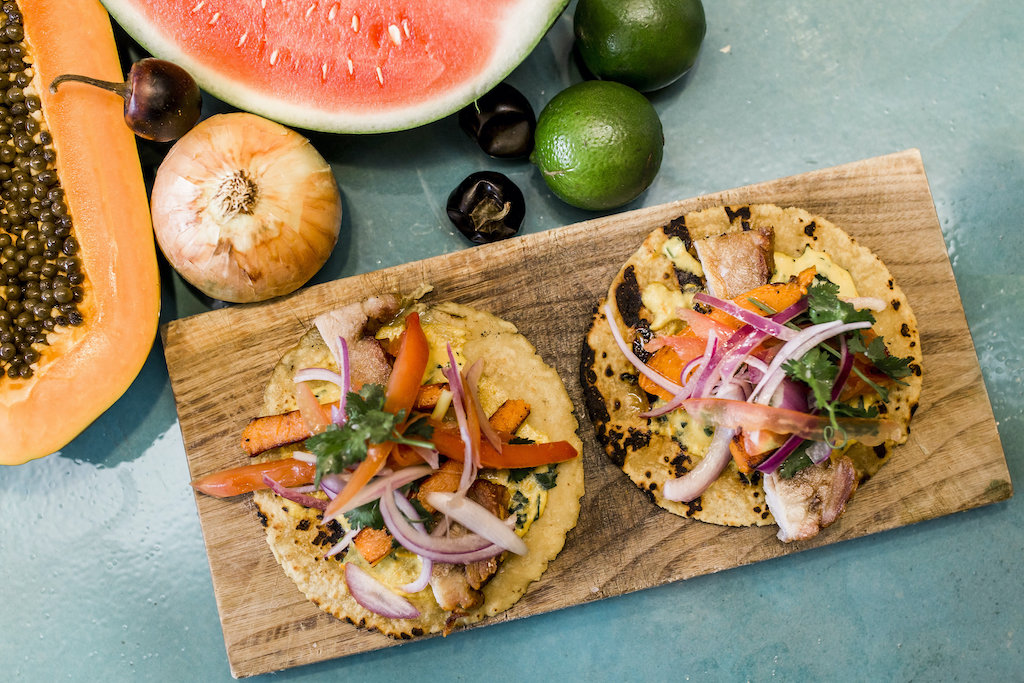 Two tacos on a wood slab with different beautiful delicious garnishes