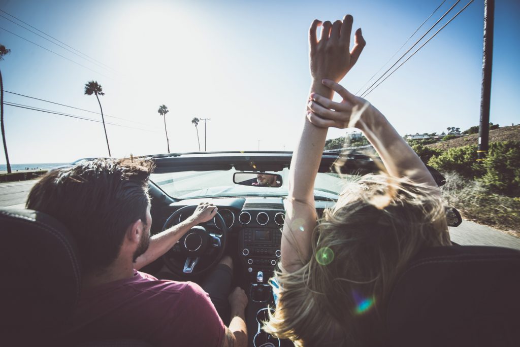 Couple in convertible car driving down the road with hands in the air