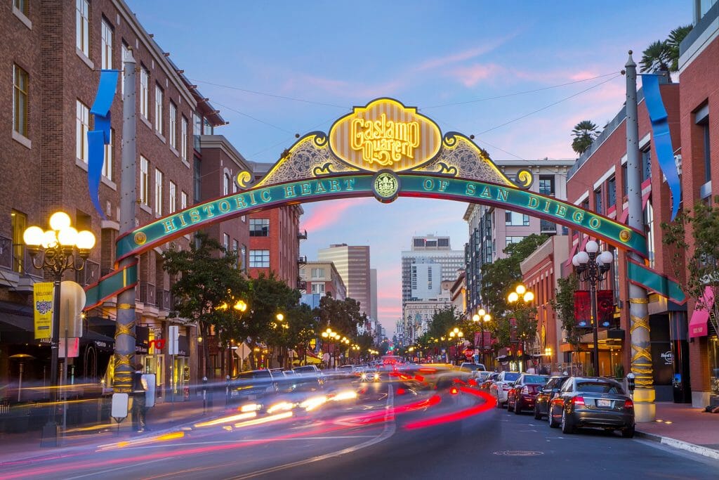 As the sun sets, cars zoom underneath the lit sign reading Gaslamp District in San Diego, California