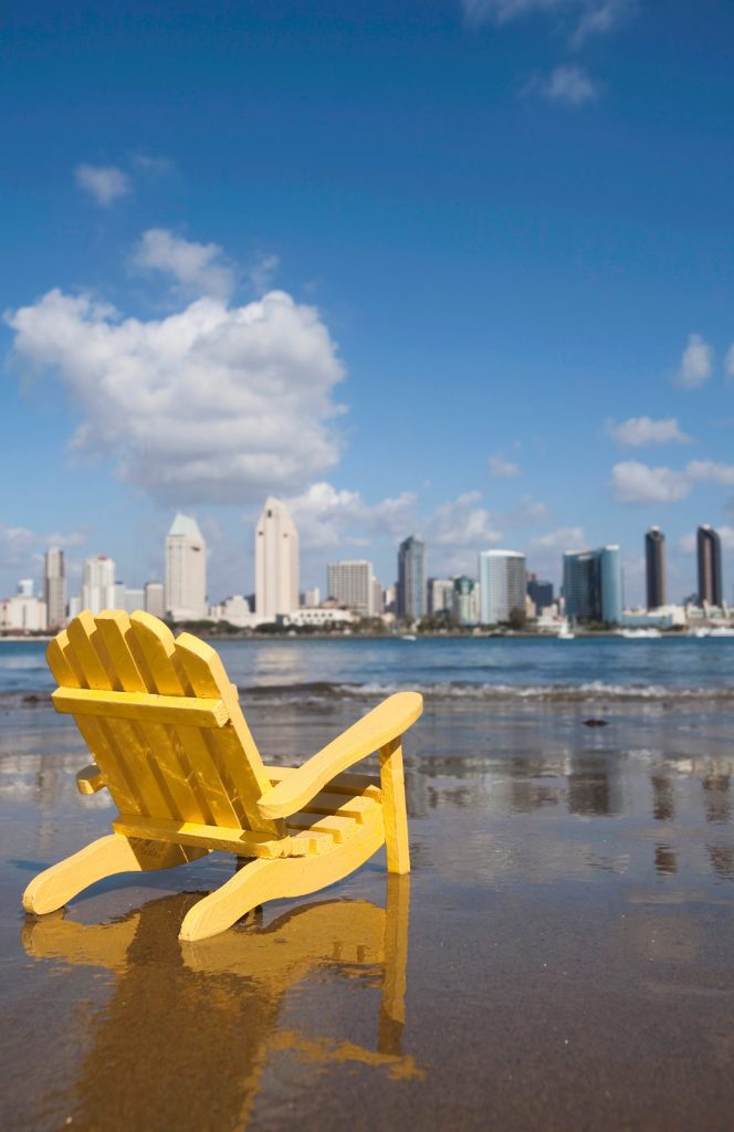 Yellow wood beach chair on the sand at a beach in Coronado with the San Diego Skyline in the Background - San Diego Staycation