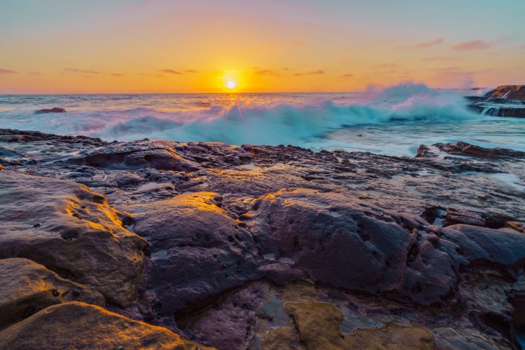 rocks on the beach at sunset with a wave crashing into them