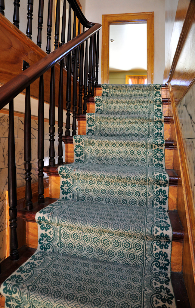 A light wood staircase with a green liner runs up to a brightly lit area of the second floor