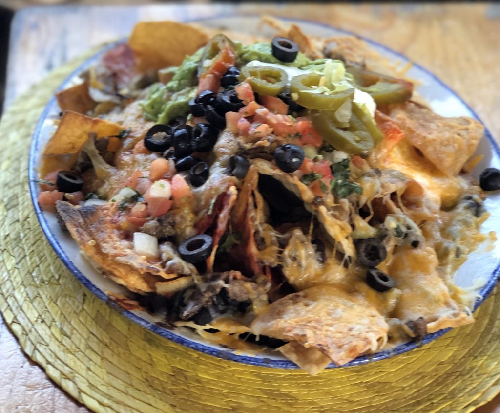 Plate with loaded nachos, including pico de gallo, guacamole, olives, cheese etc