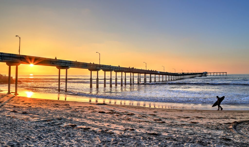 A surfer walks on Ocean Beach near the pier in San Diego, California.