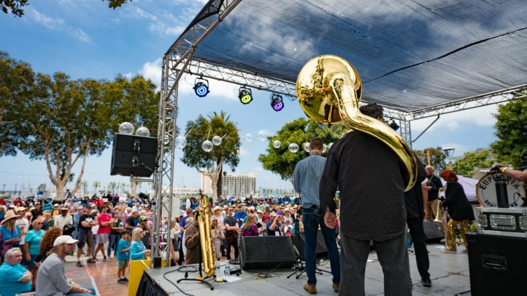 photo from behind a concert stage, with musicians from the back, crowd dancing in front of the stage outside