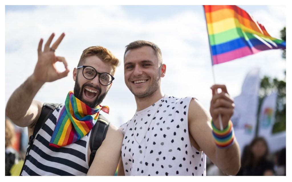 Two guys smiling and waving a rainbow flag