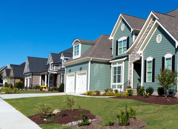 Row of modern two-story housing with well-maintained lawns and two-car garages on a sunny day.