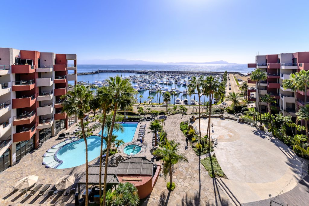 Hotel balcony views overlooking hotel pool, palm trees, and marina full of boats on sunny day. Hotel Coral y Marina, Ensenada, Mexico hotels.