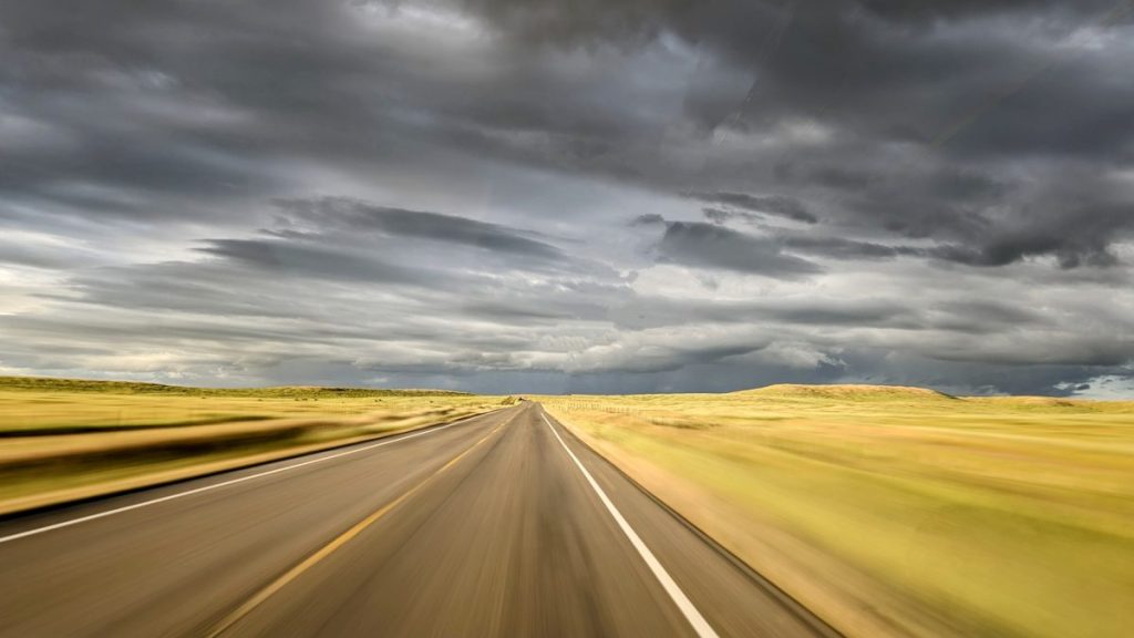 view of the road through golden green fields with a stormy sky