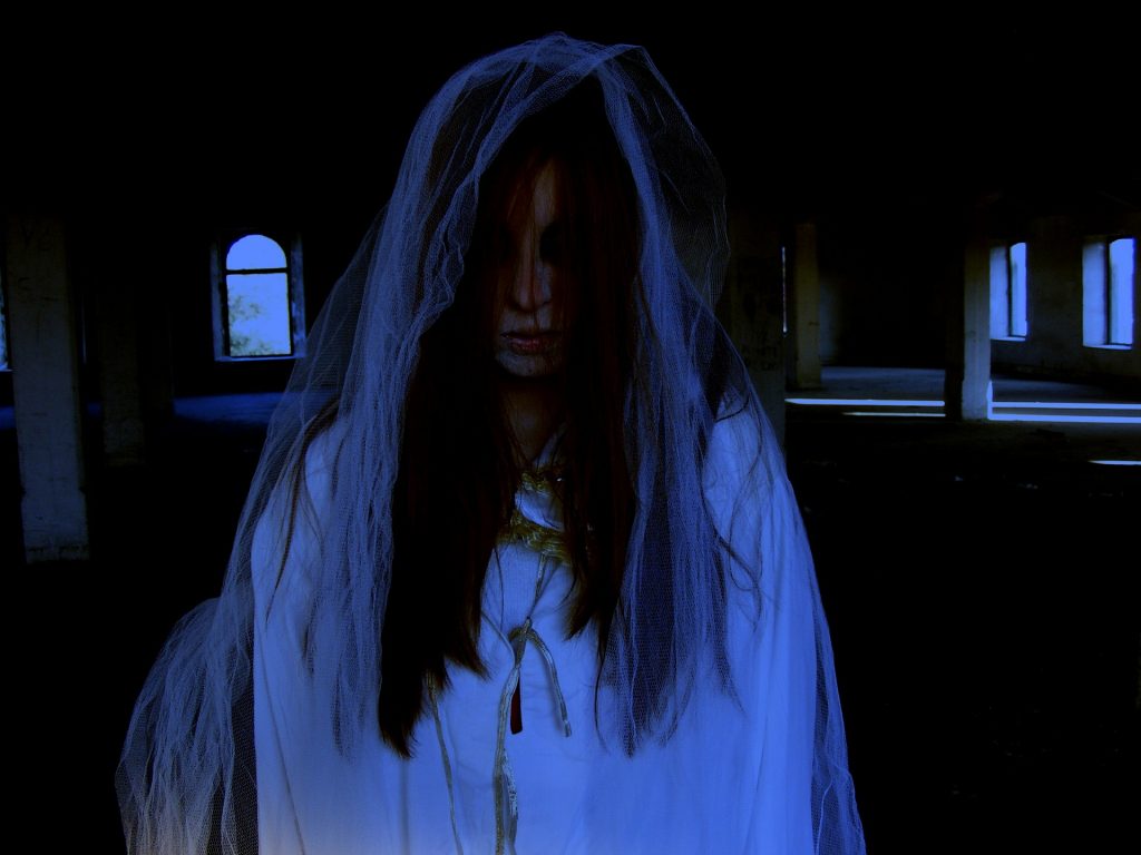 Ghostly woman dressed in white with a veil sadly draped over her head as blood drips from her forehead