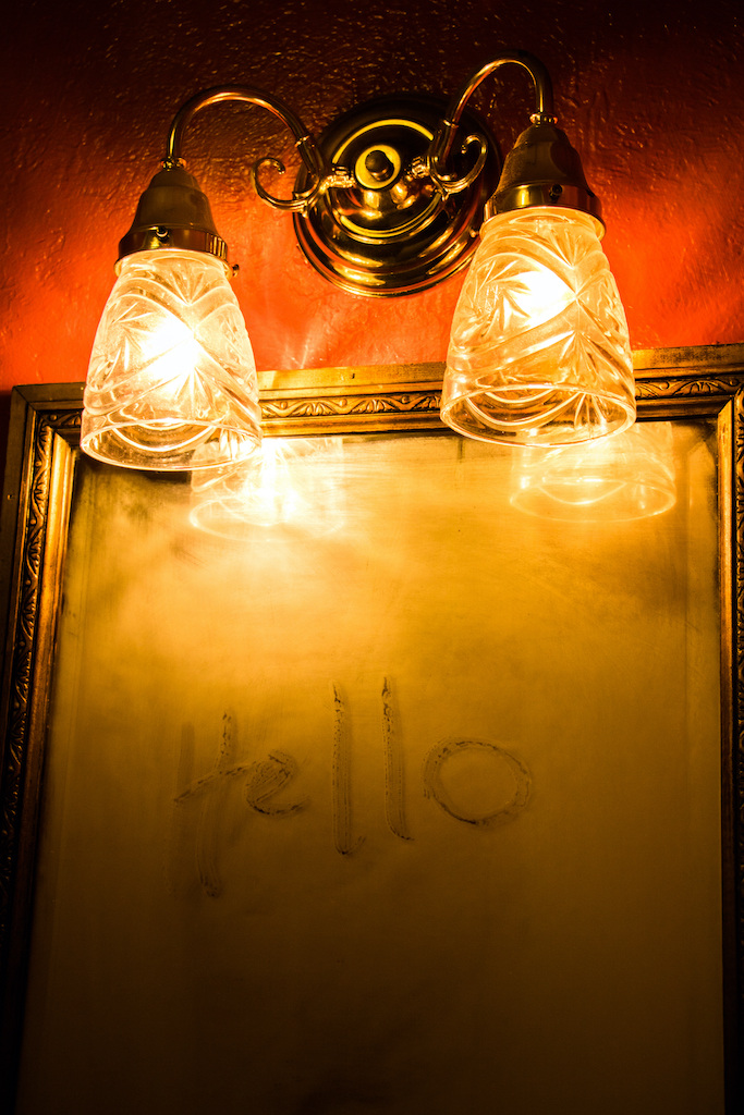 A mirror with ghostly writing on it, light dimly by the lamps overhead