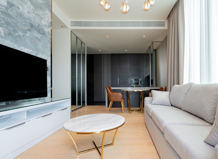 Modern living area featuring a gray sofa, white marble coffee table, and wall-mounted TV. Adjacent is a dining space with brown chairs, seamlessly designed to create an inviting atmosphere perfect for generating income through short-term rentals. A small kitchen completes the background.