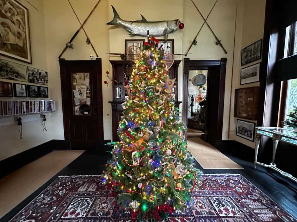 A christmas tree set up in a small room with two fake fish crossed behind the tree on the wall