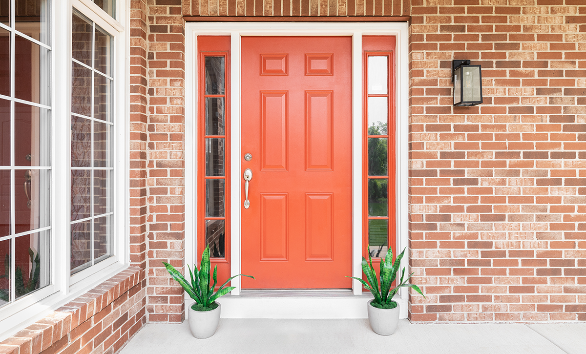 Orange front door of a brick house with potted plants on either side