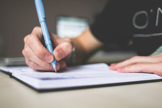 Person holding a blue pen and writing in a notebook