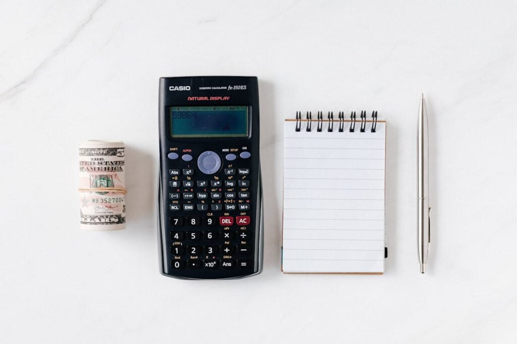 Dollar bills, calculator, notepad, and a pen on a white surface