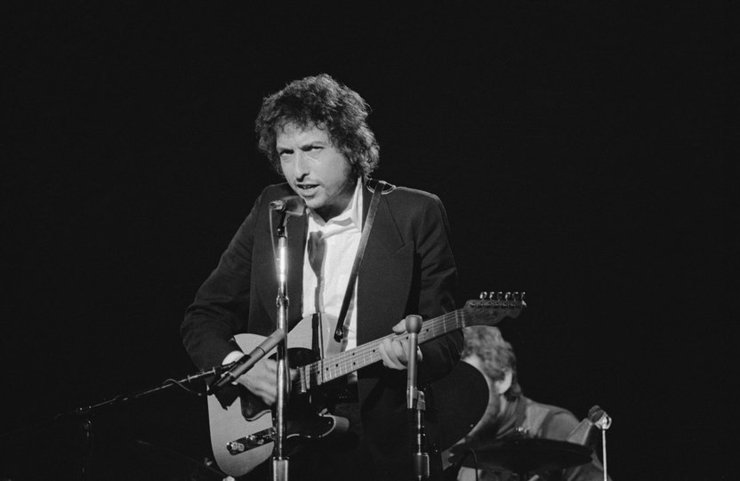 (Original Caption) Singer Bob Dylan strums out a tune on his guitar during his performance before a sell-out crowd at Boston Garden. The popular singer is making his 1st national tour in 8 years. Bob is shown with his head tilted down.