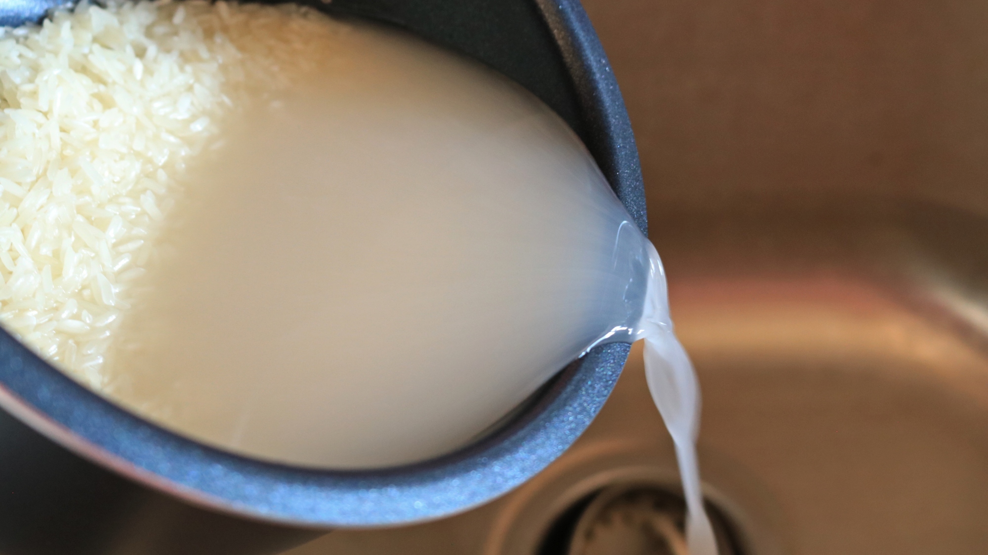 Pouring water out of a pot of rice into a sink.