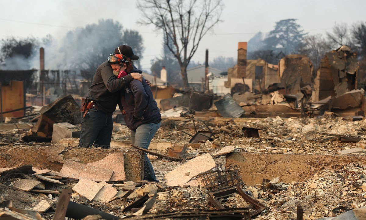 A couple embrace in front of their destroyed home from the LA wildfires