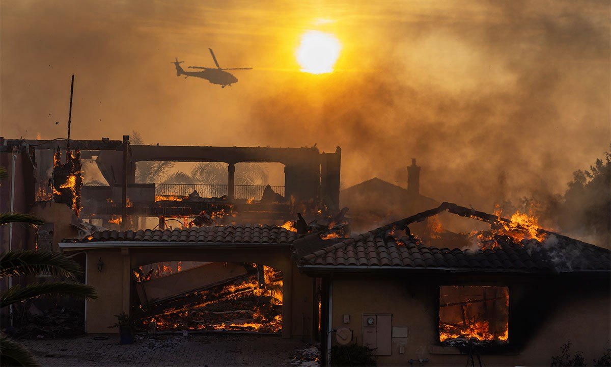 A firefighting helicopter flies near as a home burns from the Mountain Fire on November 6, 2024 in Camarillo, California. Pushed by strong winds, the fire has burned across more than 10,000 acres since it began this morning.