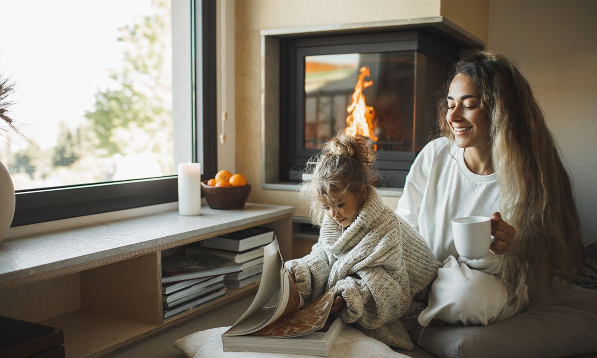 A mother and her daughter looking through a book by their fireplace at home.