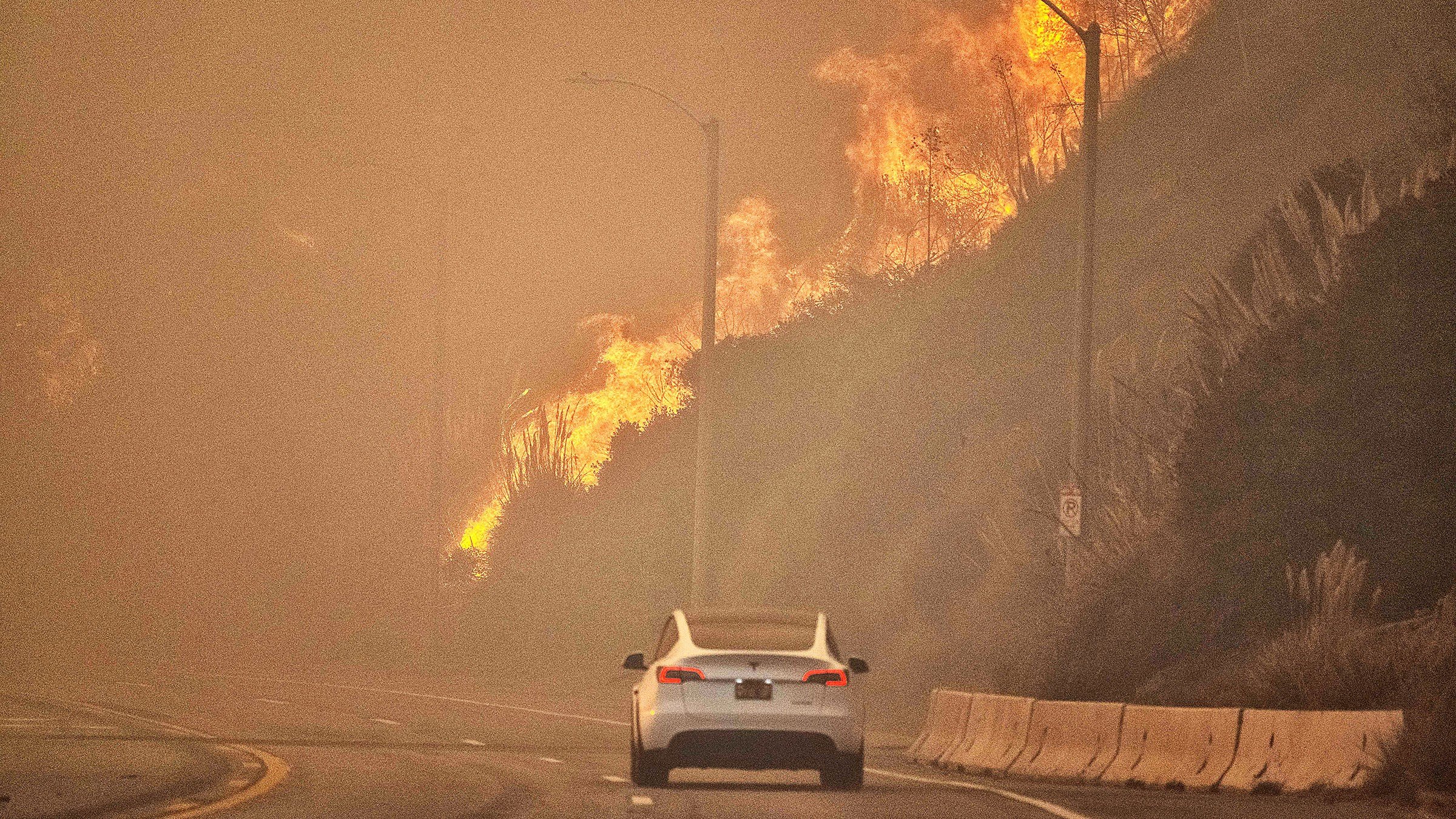 A car drives along PCH as the Palisades Fire burns in Pacific Palisades