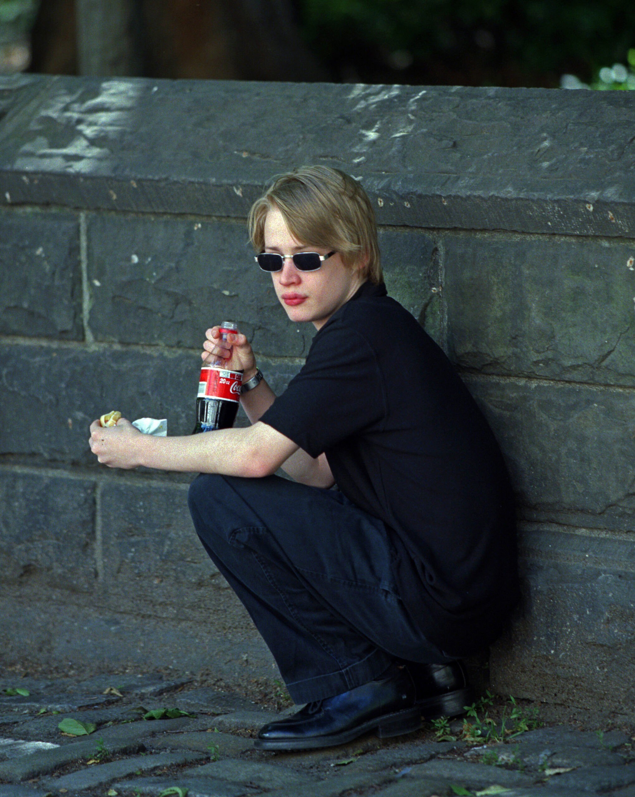 Macaulay Culkin squats on Fifth Avenue near the Metropolitan Museum to eat a hotdog and drink Coca Cola. (Photo by Lawrence Schwartzwald/Sygma via Getty Images)