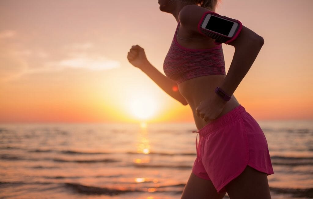 Woman in pink shorts jogging on the beach during sunset