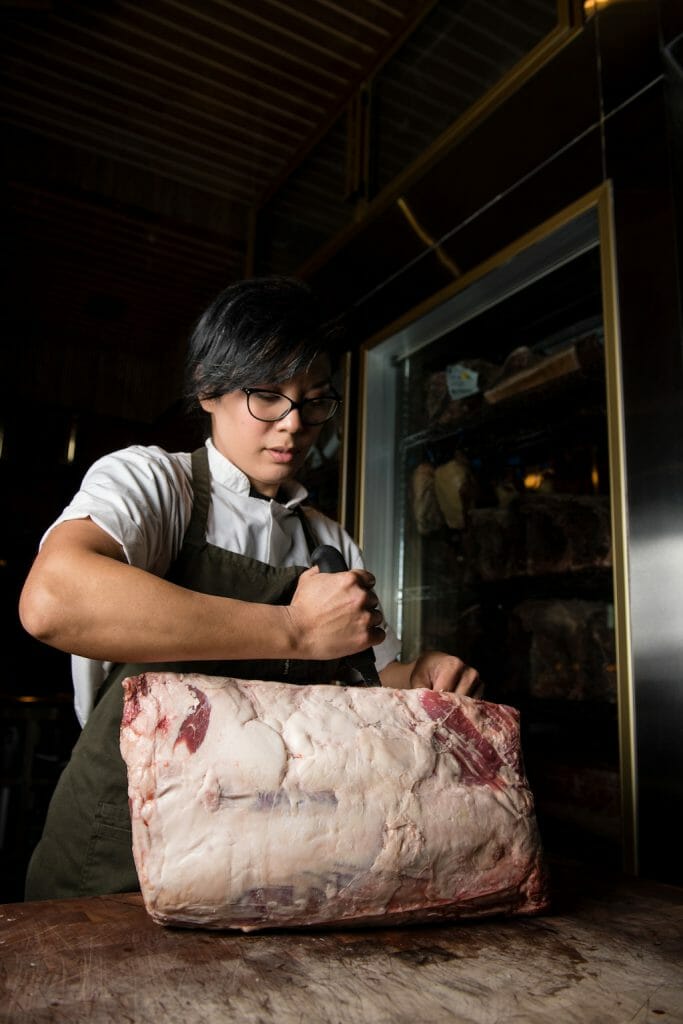 Woman using her chef knife to carve into a raw hunk of meat with power and determination