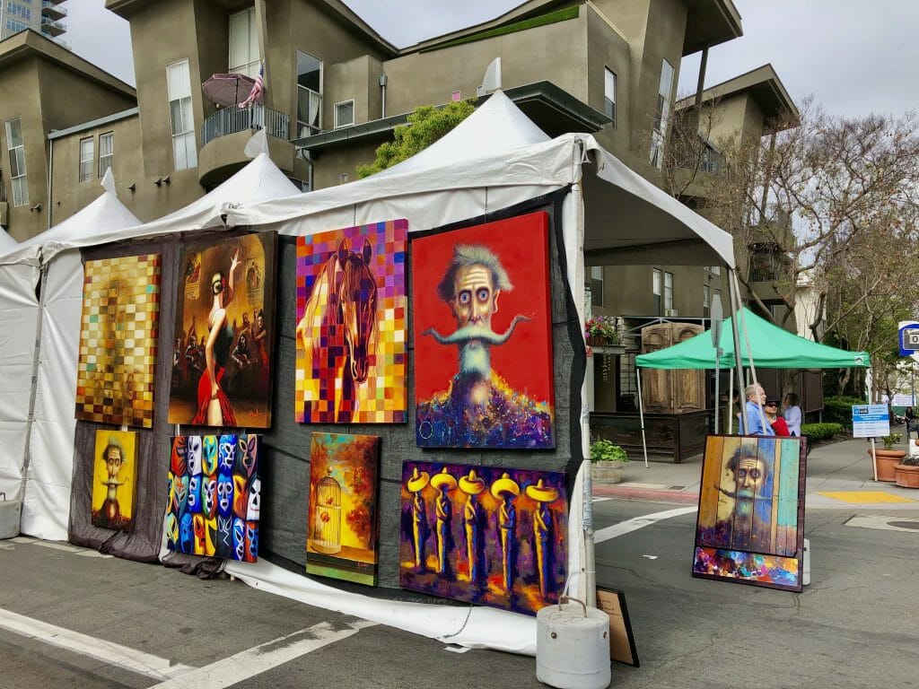 White market booths with colorful modern art  hung on the outside walls at Art Walk Little Italy