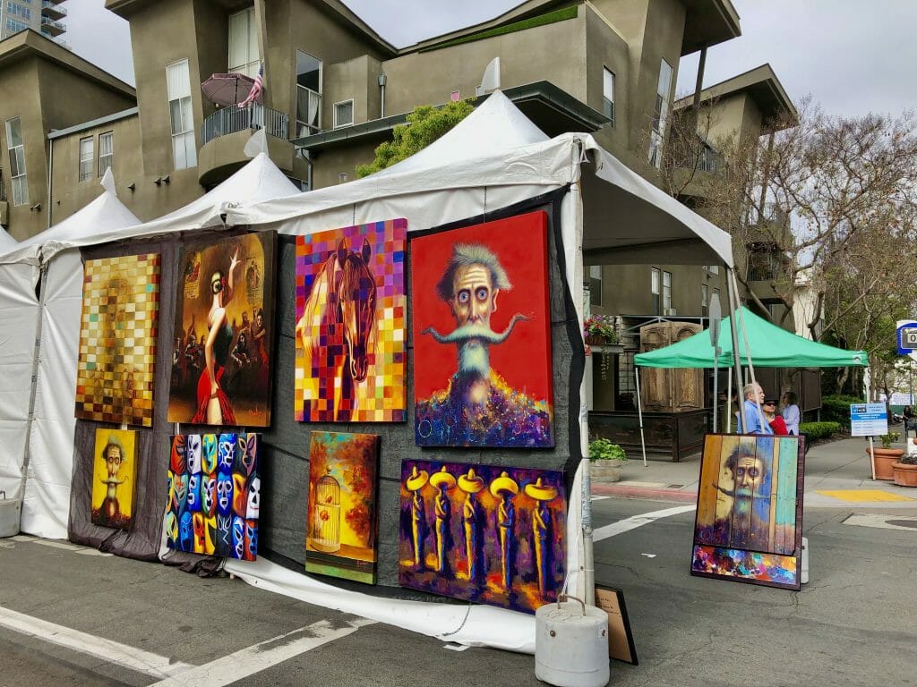 White market booths with colorful modern art hung on the outside walls at Art Walk Little Italy