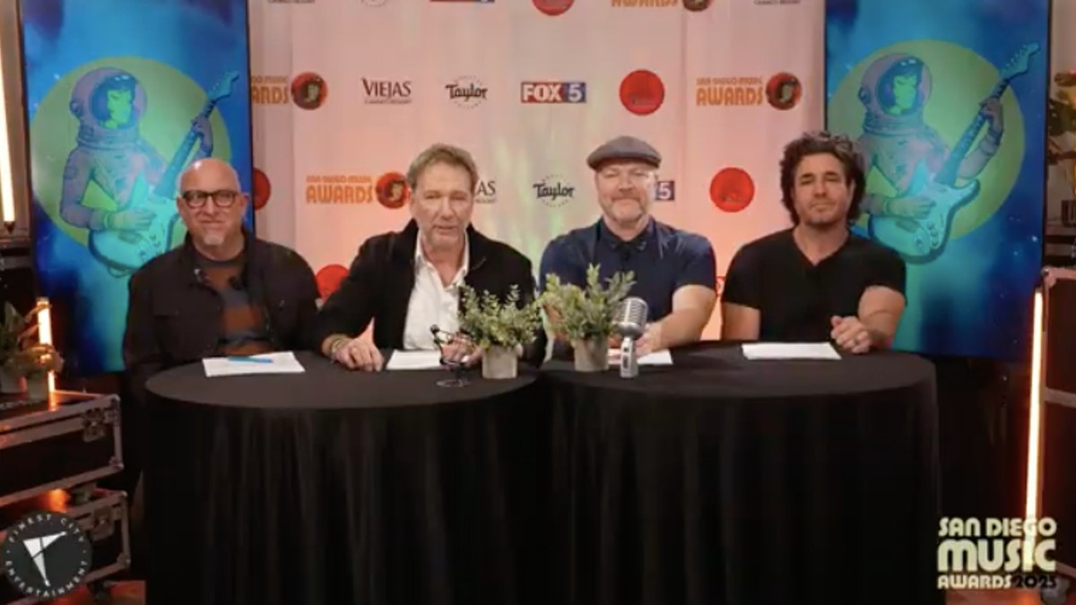 Four men seated at a table with microphones and plants, in front of a "San Diego Music Awards" backdrop.