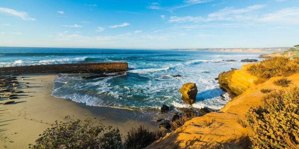 View of La Jolla Beach with a concrete fortification and cliffs surrounding a small sand beach with sea lions 