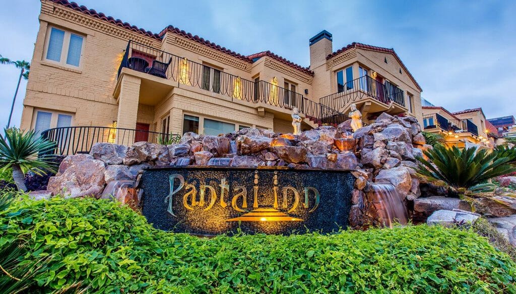 Pantai Inn La Jolla sign in front of stone wall and yellow luxury hotel in the background