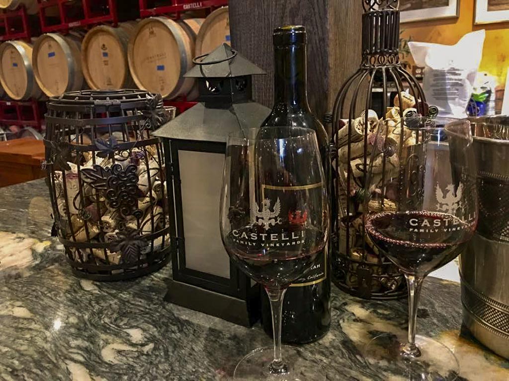 counter with wine glasses and bottles on the counter with wooden wine barrels in the background at Castelli Family Vineyards