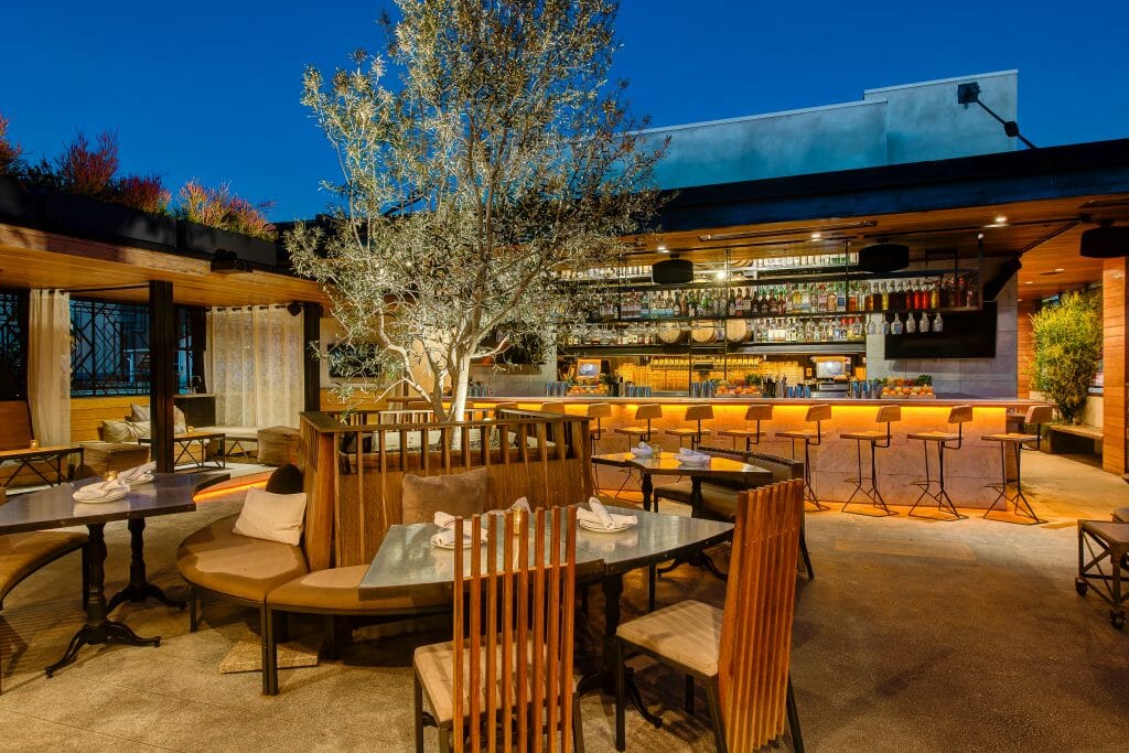 forground table with 4 chairs, background bar and lounge cabanas separated by white curtains.