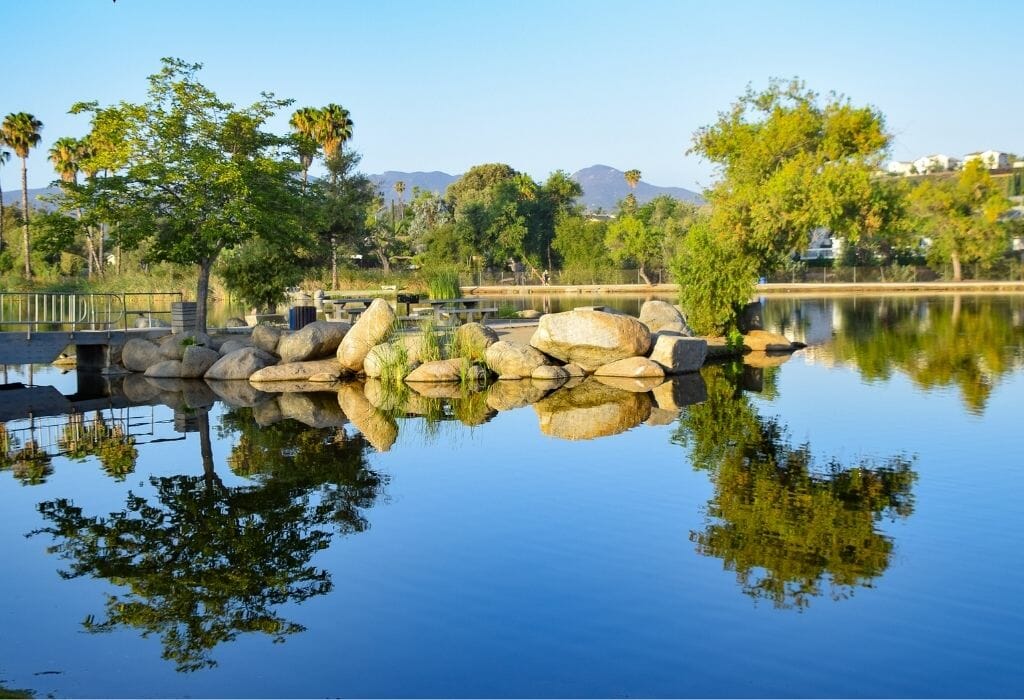 still lake with reflections of trees and boulders on a sunny day