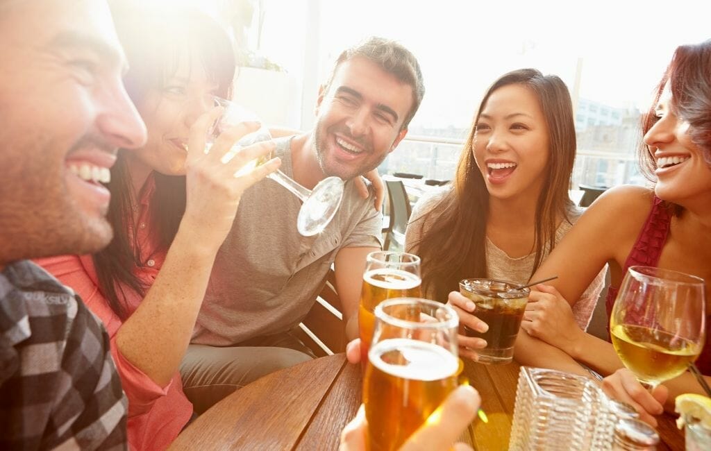 5 young people 3female 2 male sitting around a round table having drinks on a rooftop bar