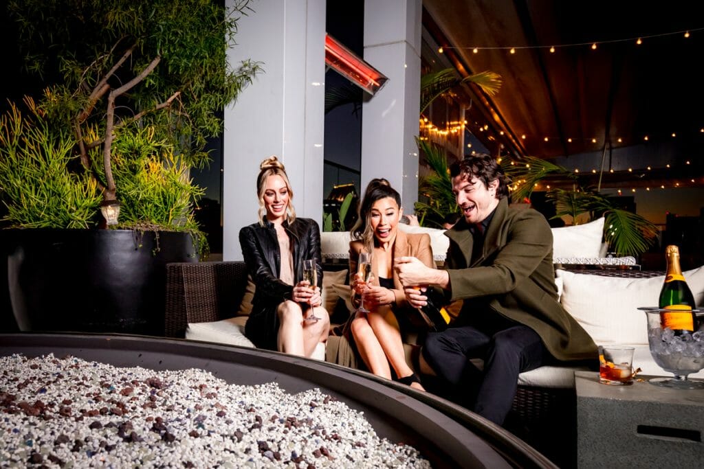 2 women and 1 man sitting by a gas fire pit at night