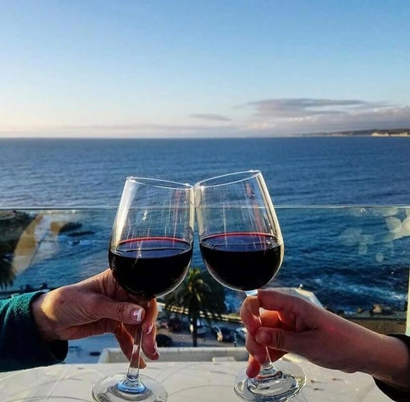 male and female hand holding stem glass with red wine toasting with an ocean view in the background during sunset at Georges at the Cove La Jolla
