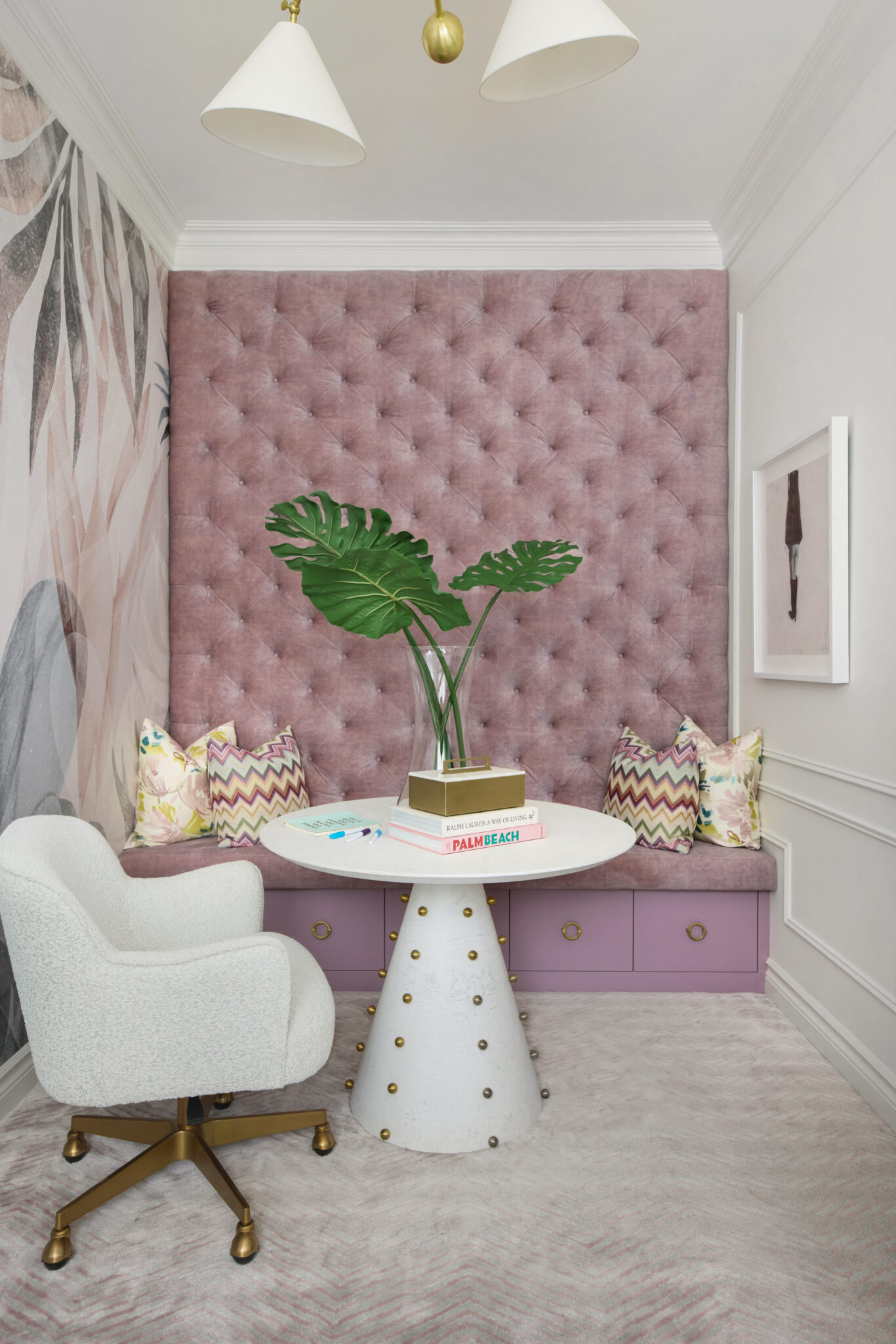 A pastel-hued space featuring a white-ash, burl-veneer, pedestal table with brass-ball details, a white chair and a rose velvet-upholstered bench seat with drawers underneath.